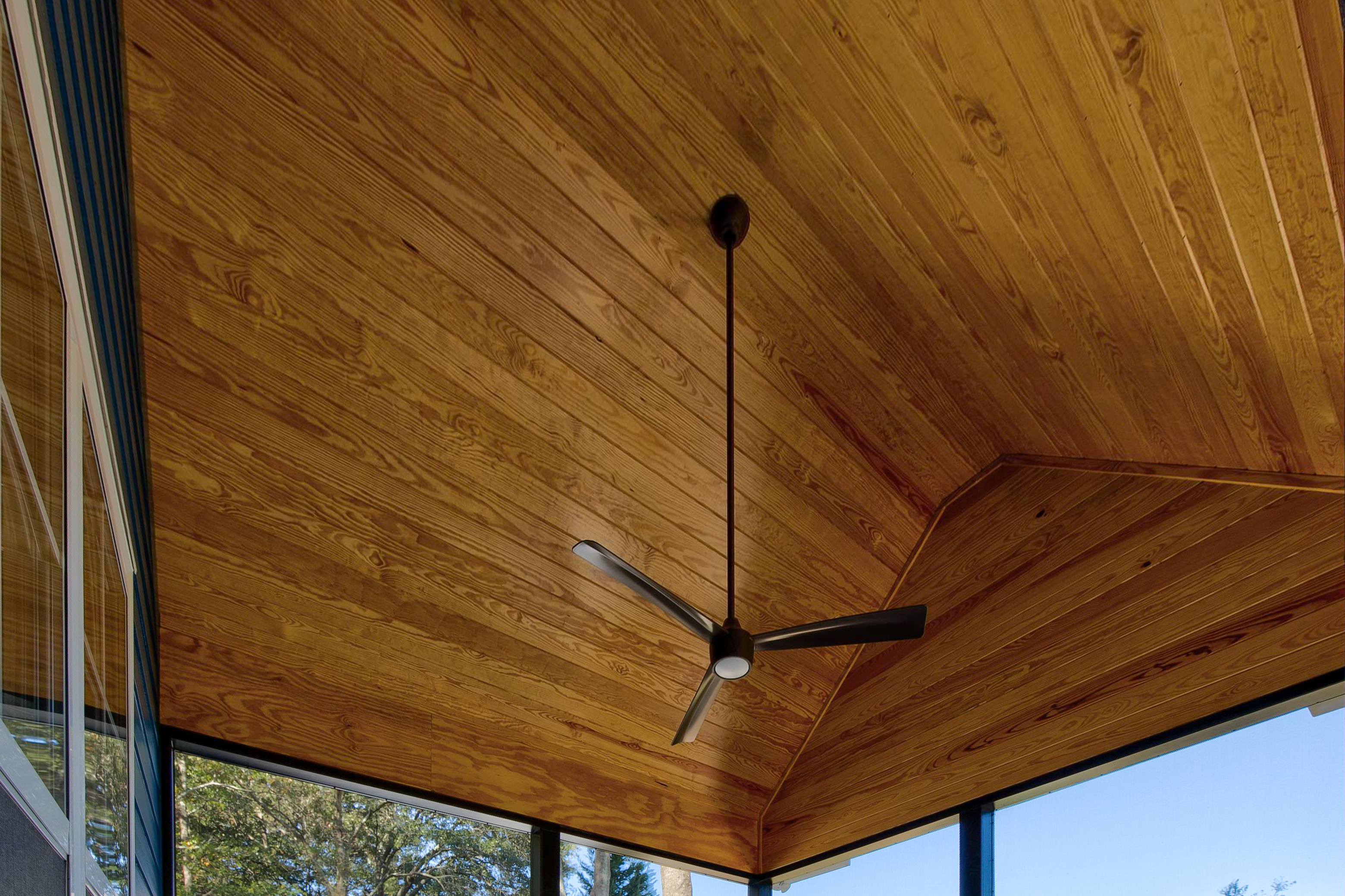 Wooden ceiling of a screened back porch with a ceiling fan. 