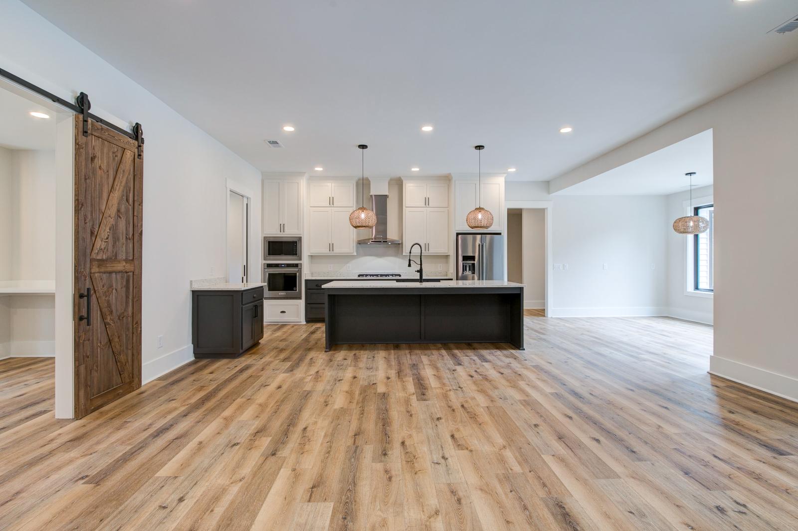 Room with white walls and wooden floors and open concept kitchen - Rafter B Construction custom home