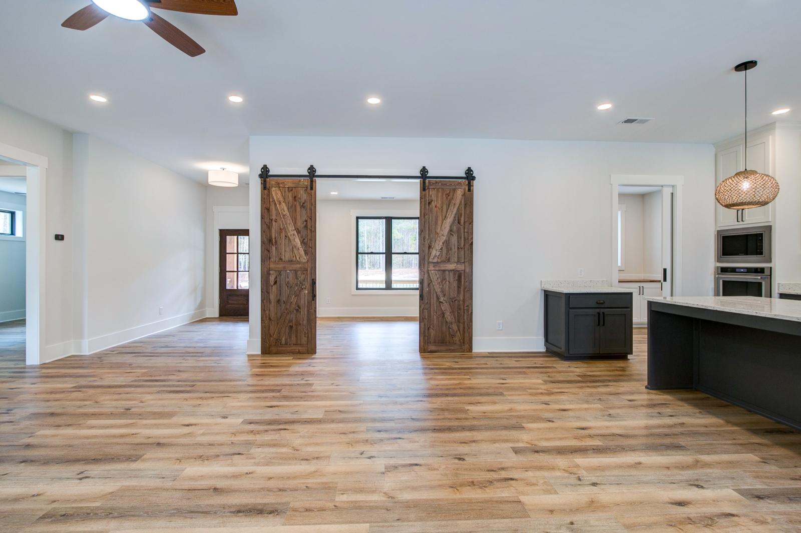 Room with white walls and wooden floors and open concept kitchen - Rafter B Construction custom home