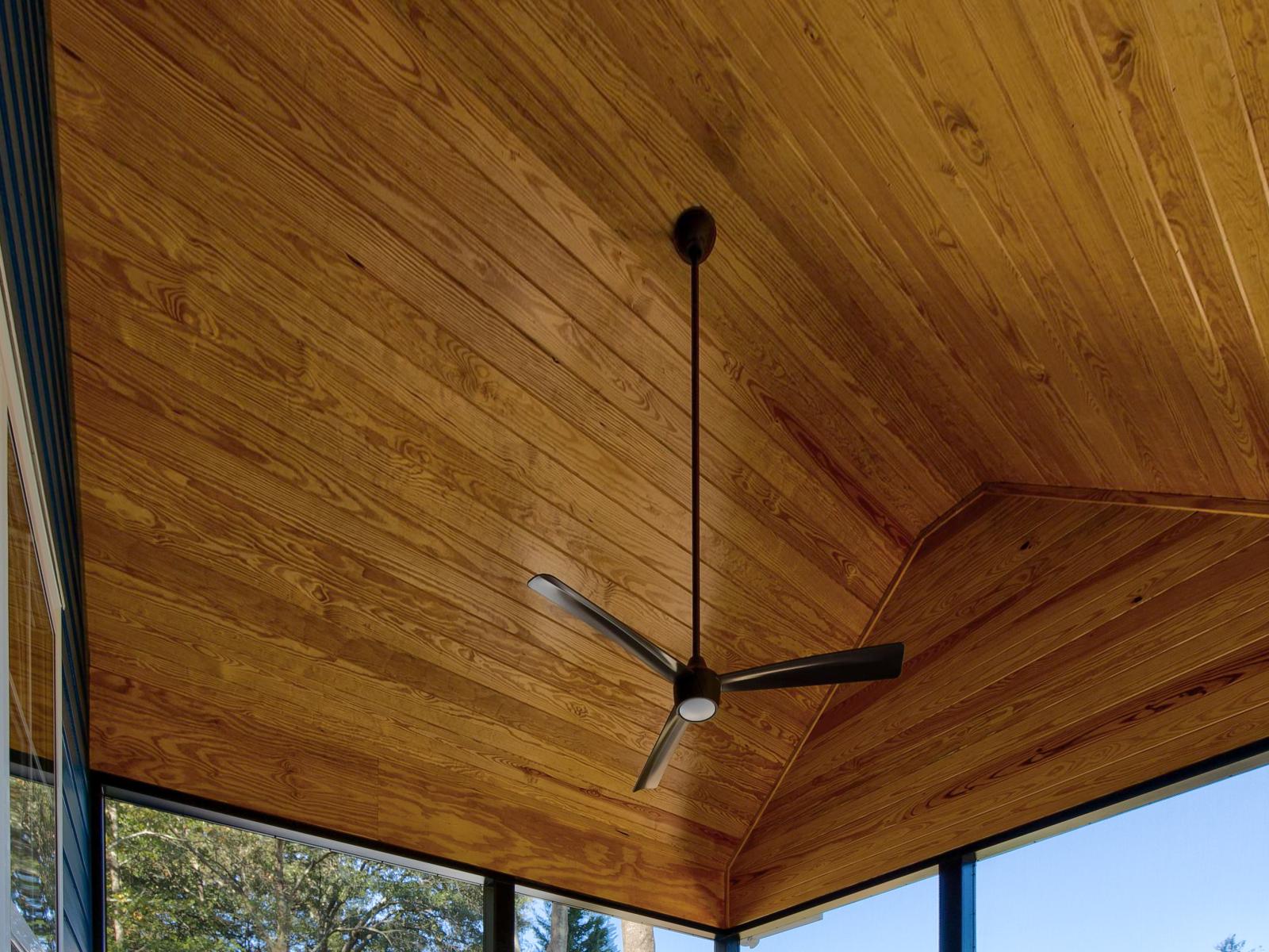 Wooden ceiling of a screened back porch with a ceiling fan.