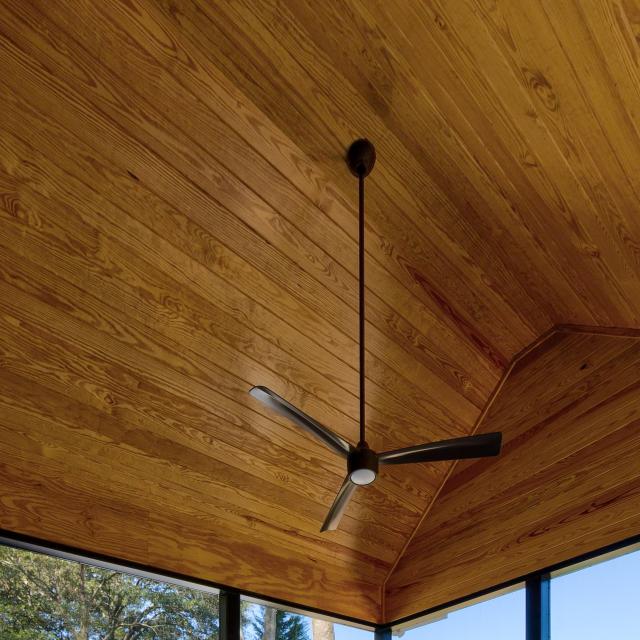 Wooden ceiling of a screened back porch with a ceiling fan.